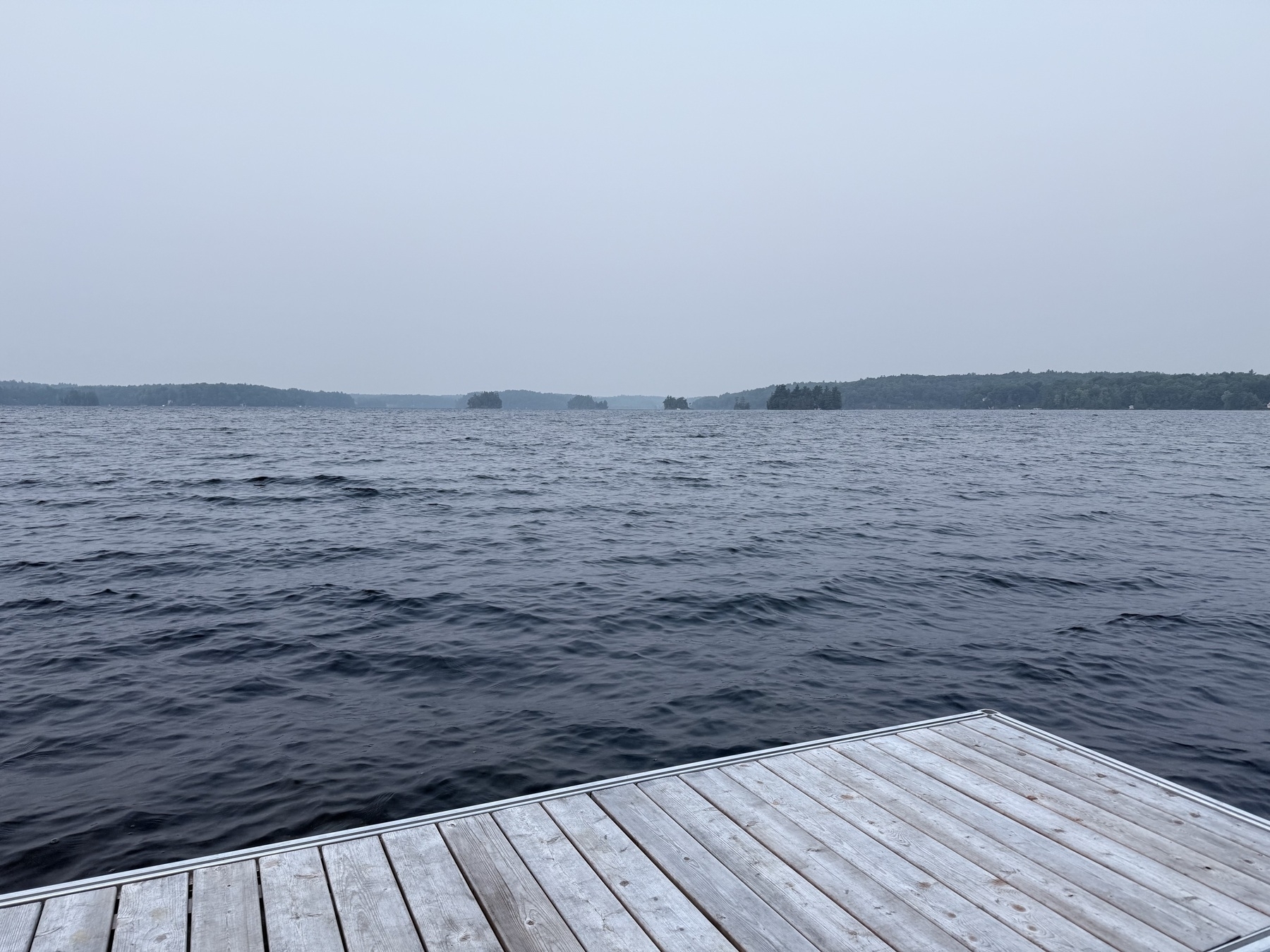 A serene lake with gentle waves is bordered by a wooden dock, under a gray, overcast sky.