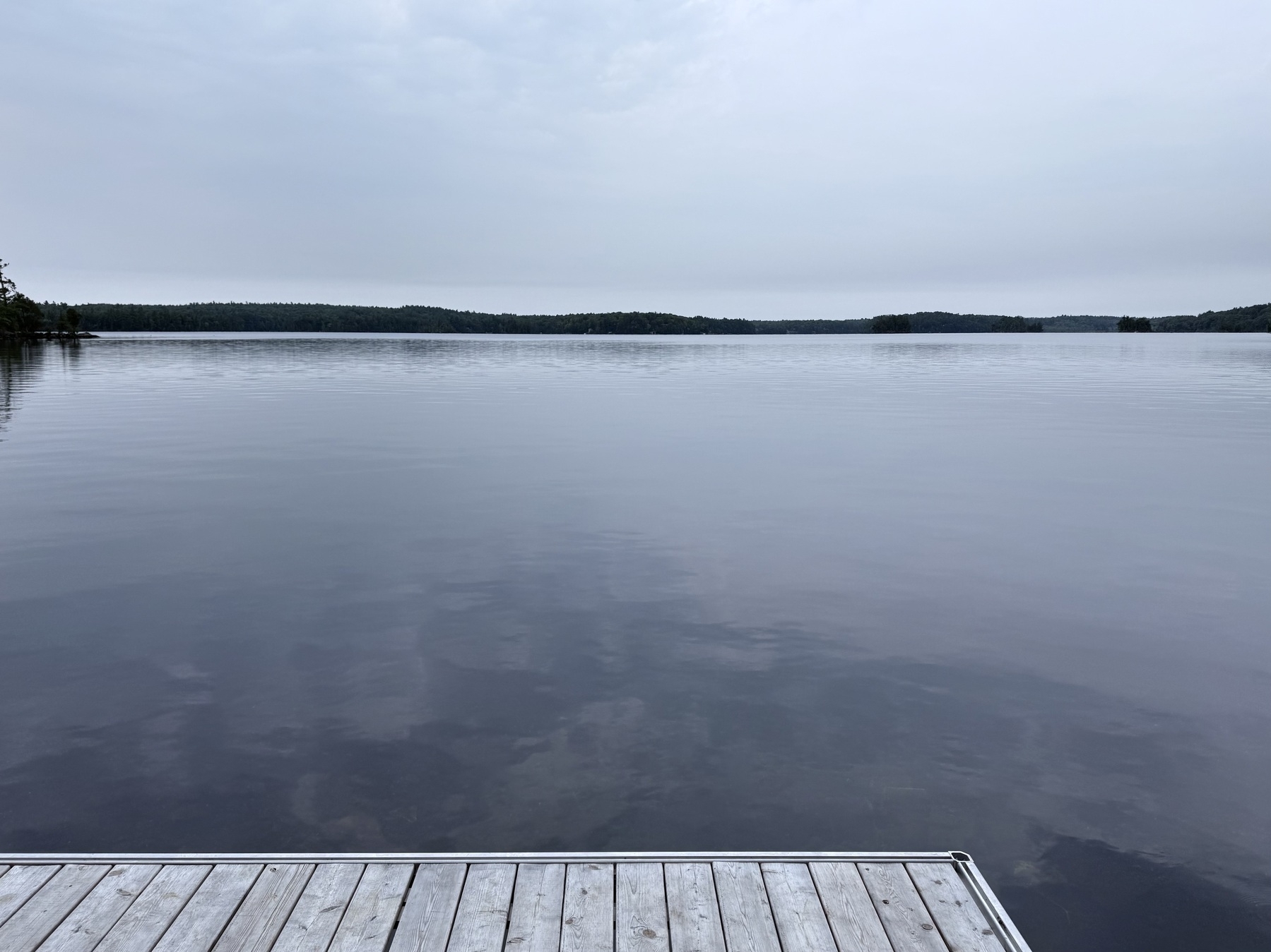 A tranquil lake with a wooden dock extending into the calm water under a cloudy sky.